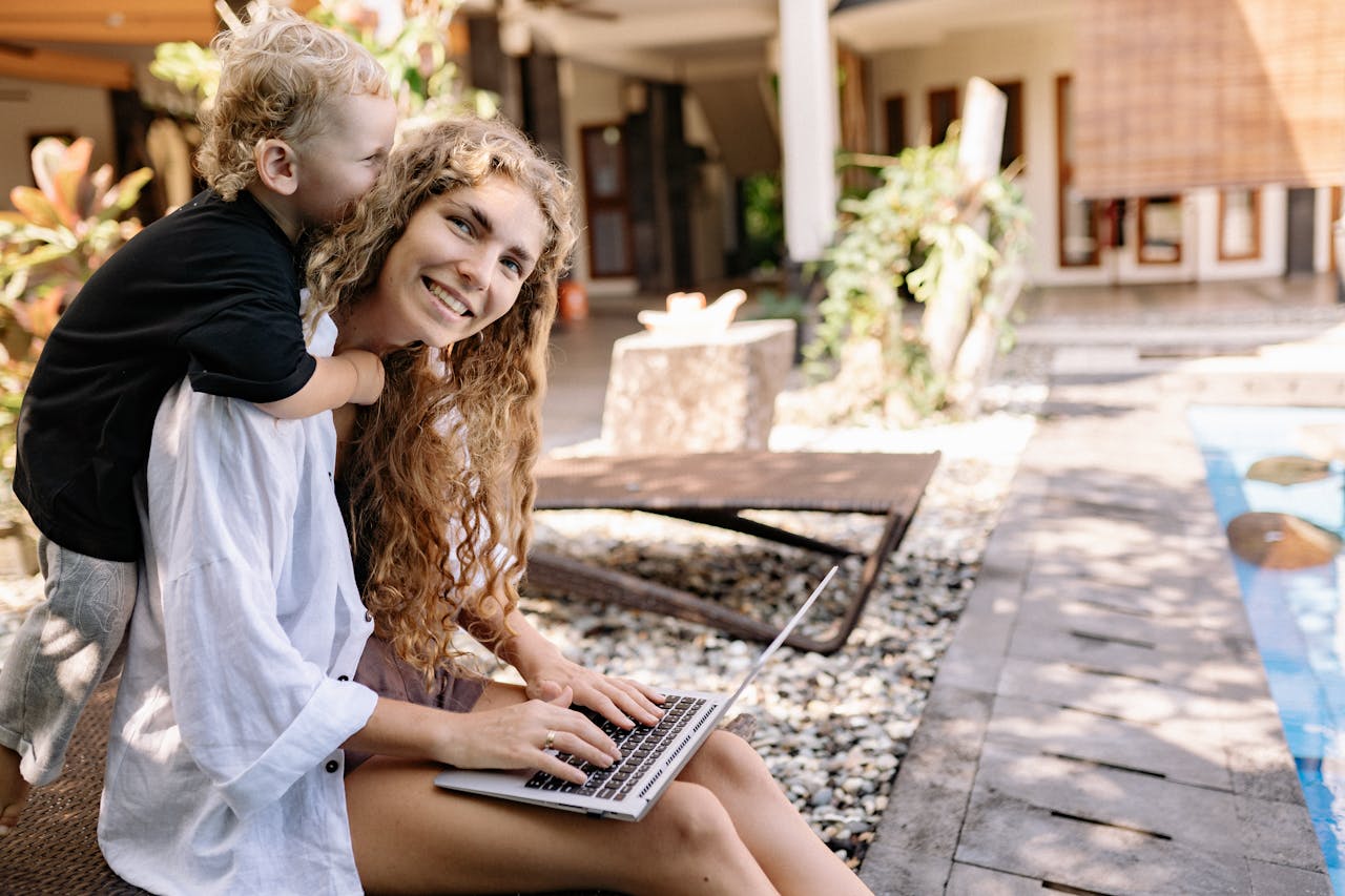 about-02 A joyful mother and child enjoying time together on a sunlit patio with a laptop.
