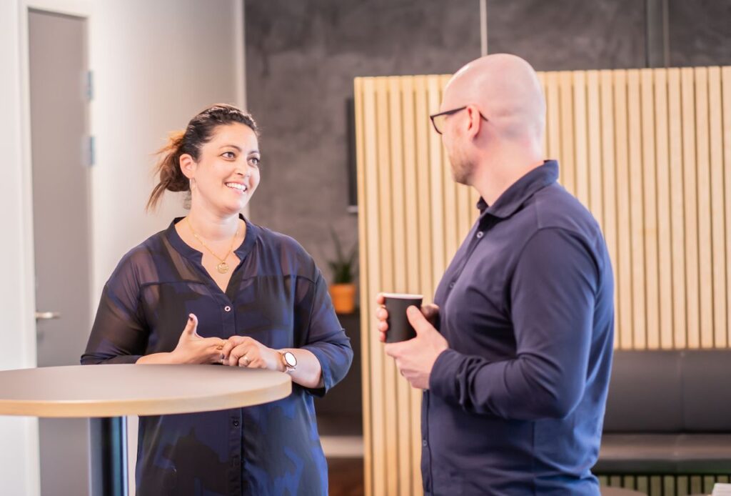 Two coworkers engage in a friendly conversation over coffee in a modern office setting.
