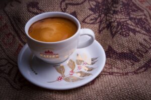 A detailed view of a coffee cup with espresso on a decorated saucer placed on burlap.